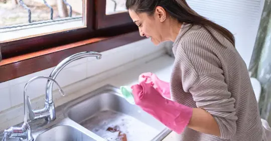 Woman Using Plunger In Kitchen Sink